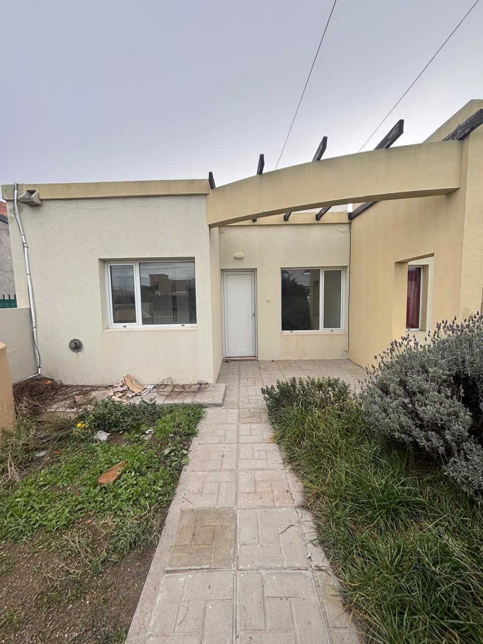 Frente de la casa con pérgola y senda de baldosas hacia la puerta