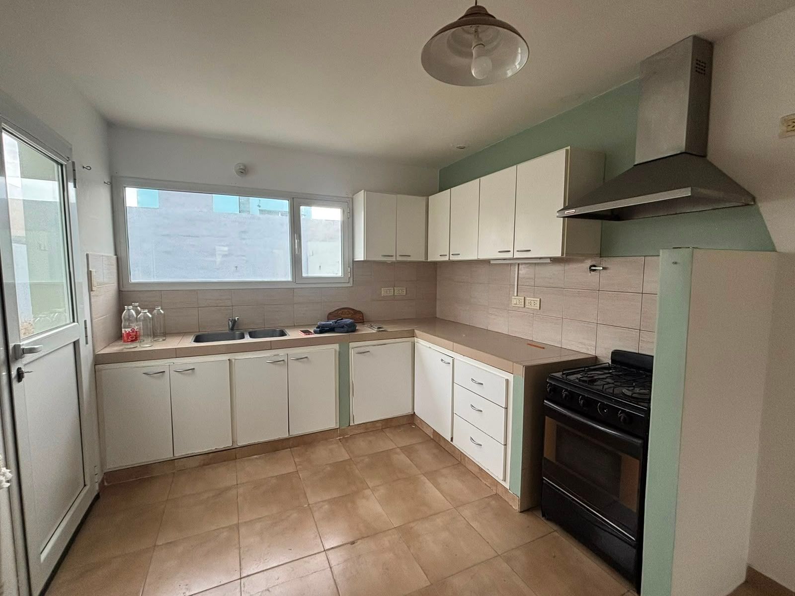 Cocina con mesada en L, alacenas blancas, campana y cocina a gas